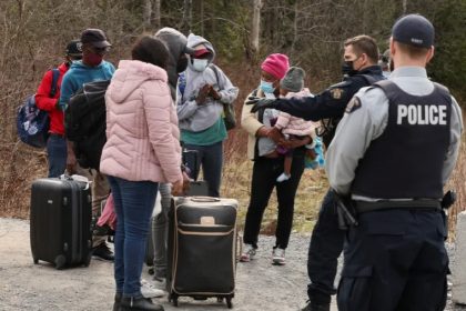 Asylum seekers talk to a police officer as they cross into Canada from the US, near a checkpoint on Roxham Road near Hemmingford, Quebec, April 24, 2022