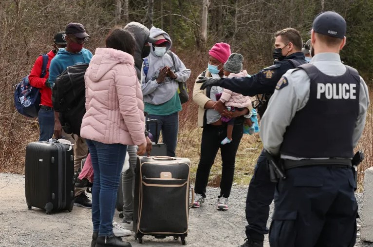 Asylum seekers talk to a police officer as they cross into Canada from the US, near a checkpoint on Roxham Road near Hemmingford, Quebec, April 24, 2022